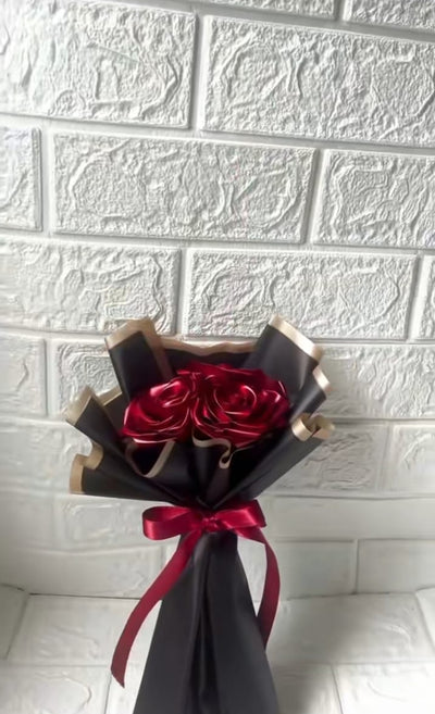 Bouquet wrapped in black paper with red ribbons against a white tiled wall.